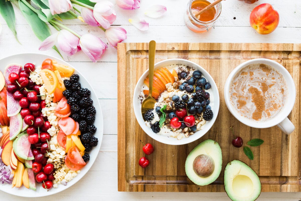 A variety of fruits on a plate next to a smoothie bowl topped with fruit and a cup of tea.