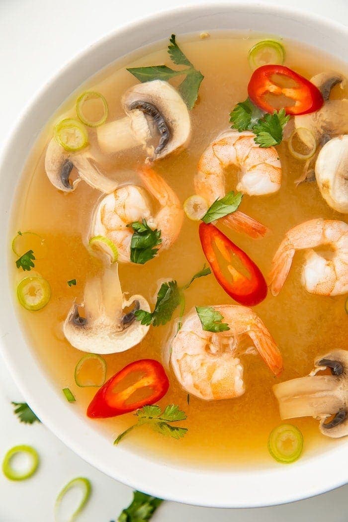 Tom yum soup in a bowl with shrimp, chilis, mushrooms, and pieces of green onion and cilantro