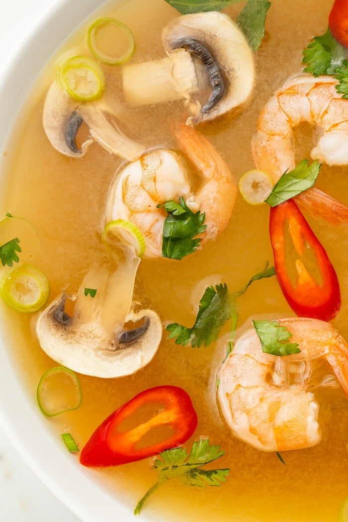 Close-up of tom yum soup in a bowl with shrimp, chilis, mushrooms, and pieces of green onion and cilantro