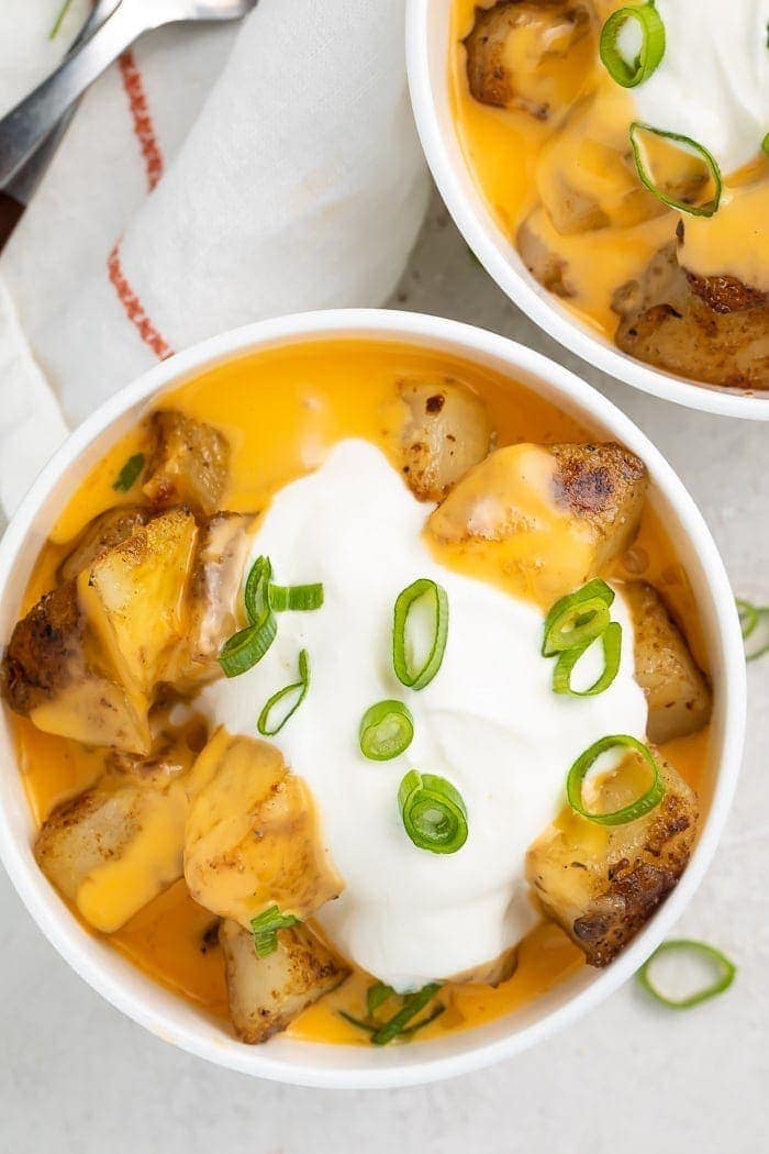Overhead shot of potato cubes in a bowl covered with nacho cheese and sour cream with sliced green onions