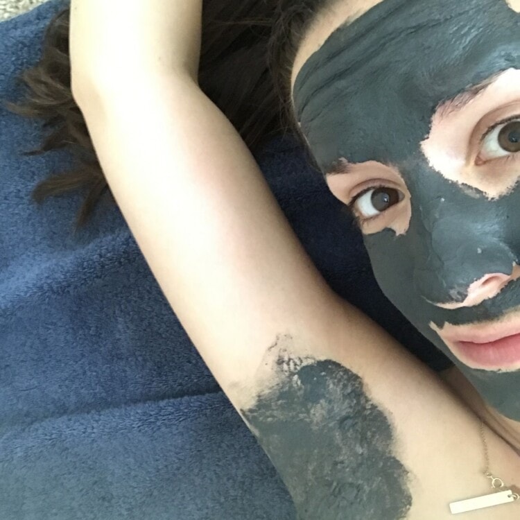Cheryl lying on a towel with her arm above her head, with a charcoal mask applied to her face and her underarm before using natural deodorant