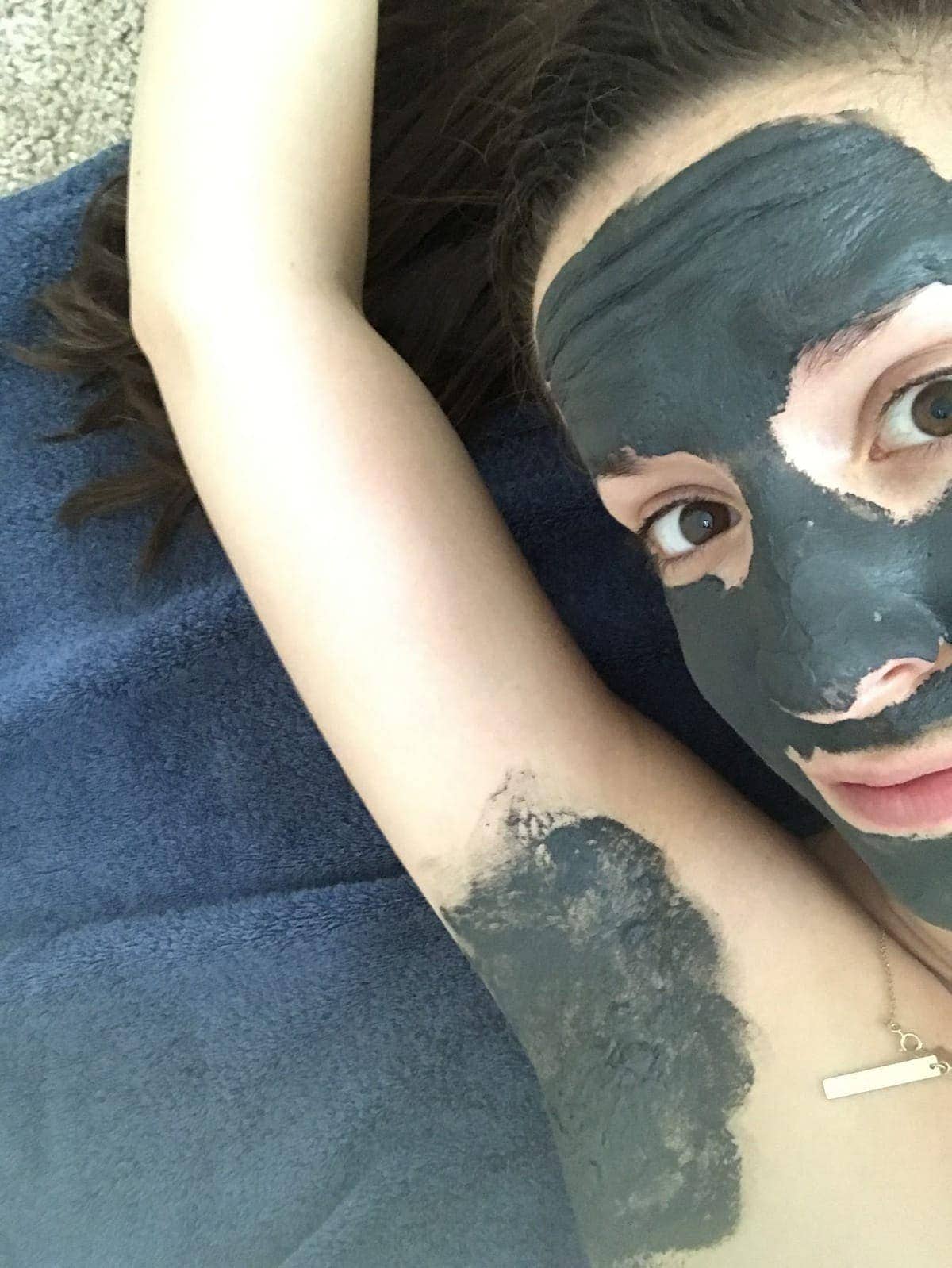 Cheryl lying on a towel with her arm above her head, with a charcoal mask applied to her face and her underarm before using natural deodorant
