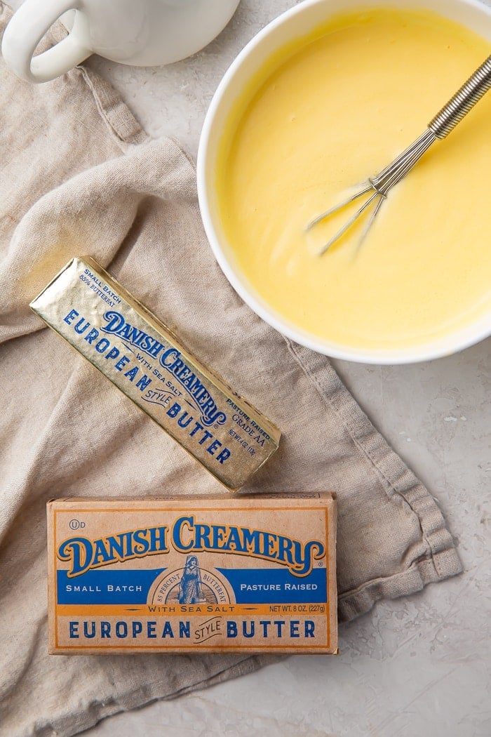 A bowl of hollandaise sauce with a whisk in it surrounded by a kraft box of butter and a stick of Danish Creamery butter