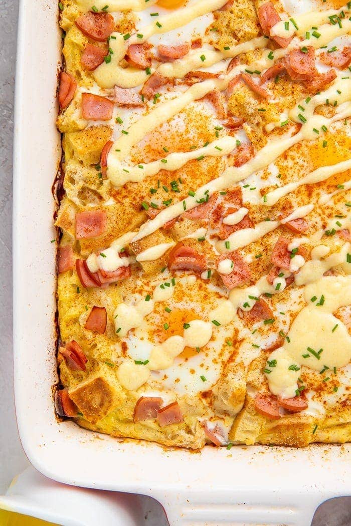 A baked eggs benedict casserole in a baking dish drizzled with a zig-zag of hollandaise sauce