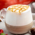 White coffee mug with coffee, whipped cream, and caramel cross-stitch drizzle