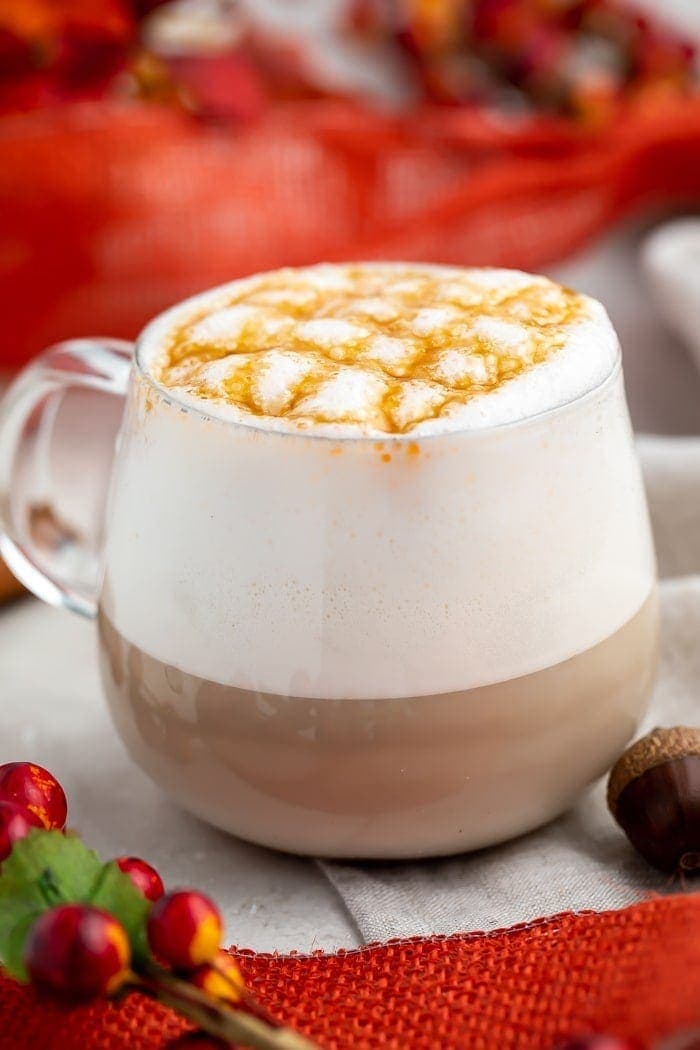 A glass mug of pumpkin caramel macchiato with lots of froth and a criss-cross design made of caramel sauce on the top