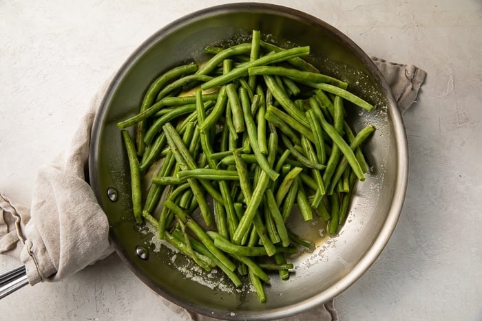 Overhead view of sauteed green beans in a large silver skillet