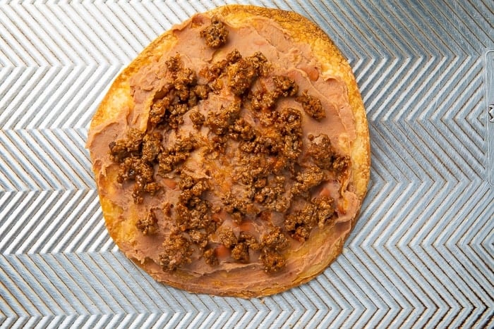 Ground beef and refried beans spread on a baking tortilla