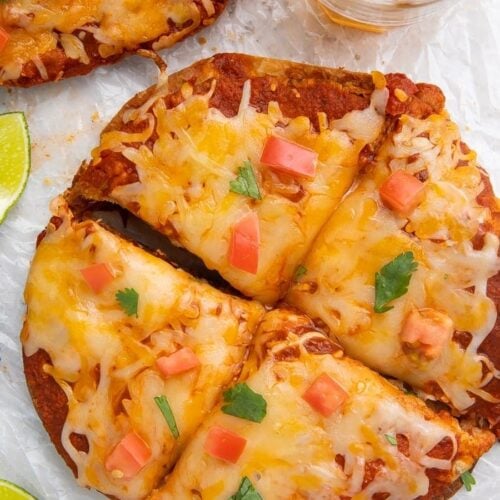 Overhead shot of Taco Bell Mexican pizza recipe topped with diced tomatoes and cilantro, surrounded by a glass of beer and lime wedges