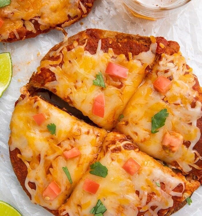 Overhead shot of Taco Bell Mexican pizza recipe topped with diced tomatoes and cilantro, surrounded by a glass of beer and lime wedges