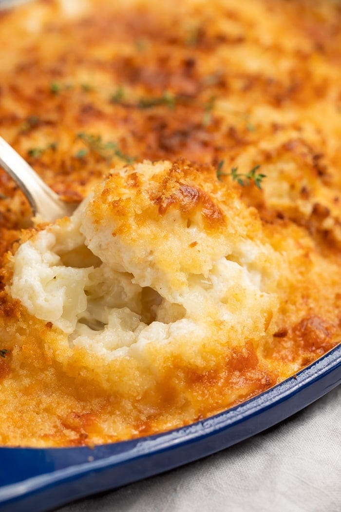 A spoonful of cauliflower au gratin being lifted from a baking dish