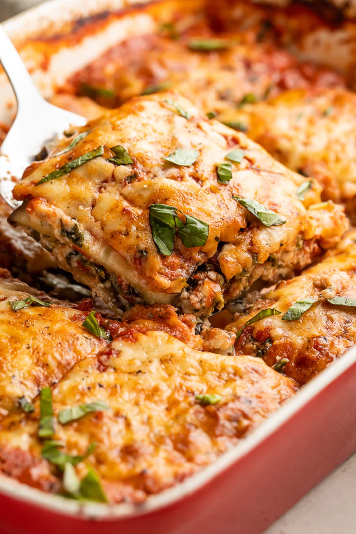 A square of eggplant lasagna being lifted out of a casserole dish of lasagna.