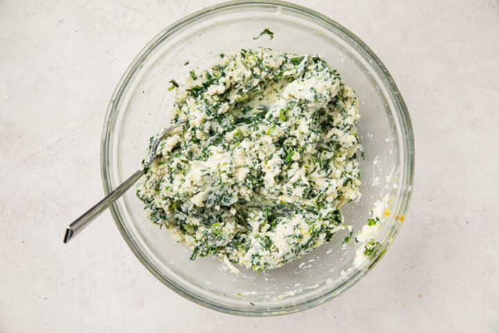 Creamy ricotta cheese and spinach filling mixture in a large glass mixing bowl.