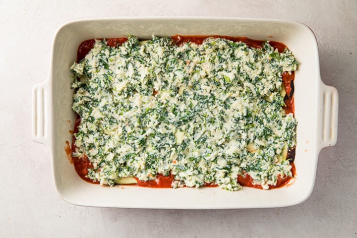Eggplant slices topped with a creamy spinach ricotta filling in a casserole dish.