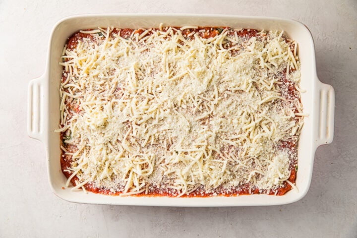 Eggplant lasagna, topped with shredded mozzarella and grated parmesan, in a rectangular white baking dish.