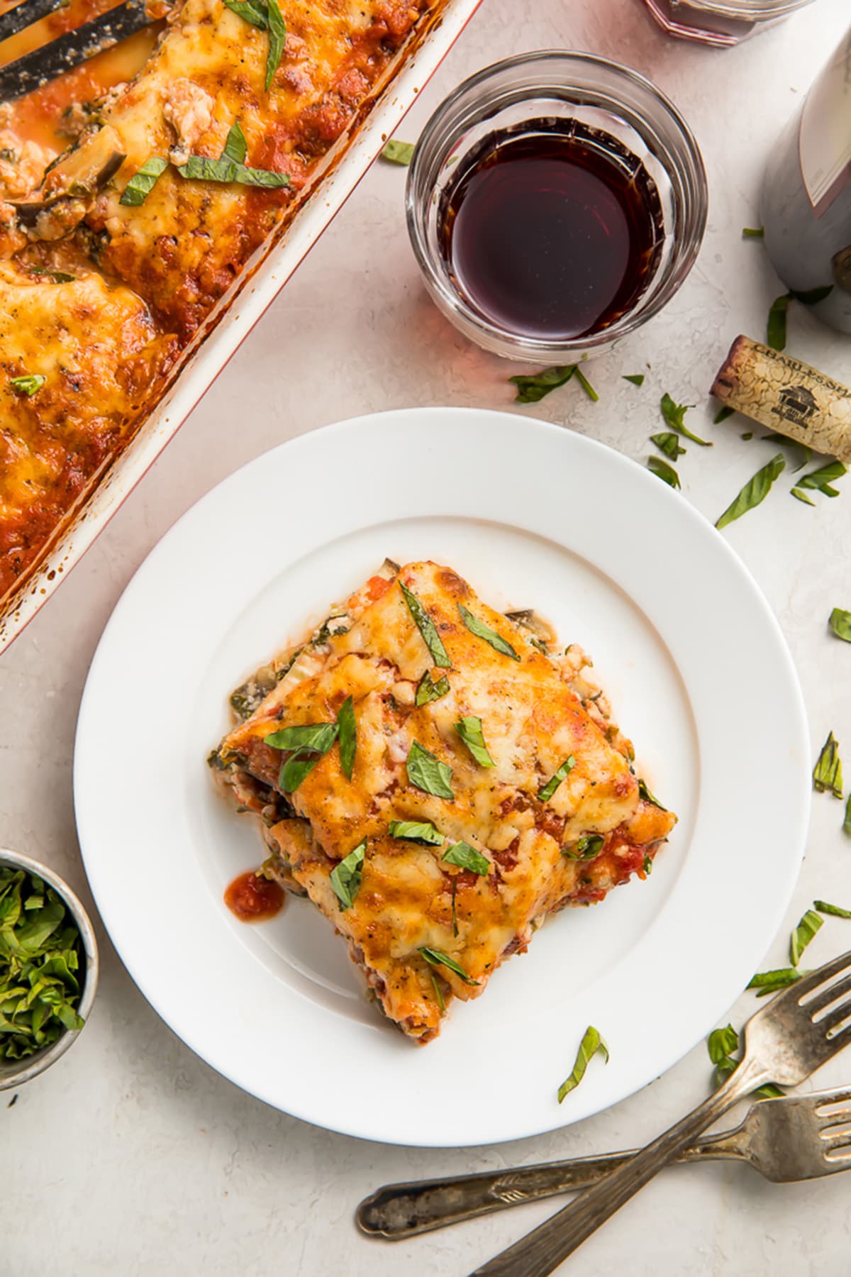 A square of eggplant lasagna on a white plate next to a casserole dish of eggplant lasagna.