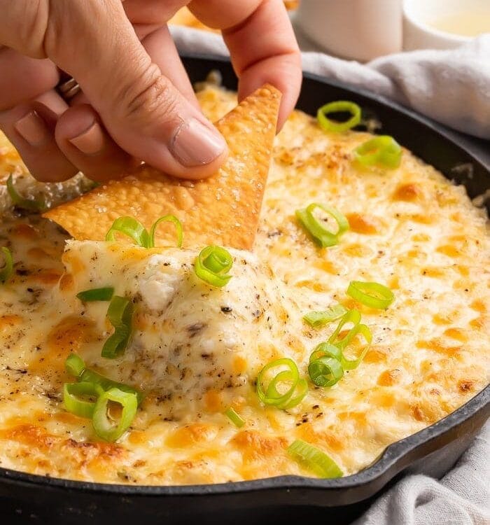 A hand dipping a chip into a cast iron skillet of crab rangoon dip