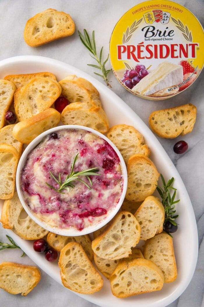 A serving tray with crackers and cranberry brie dip with a package of President Brie