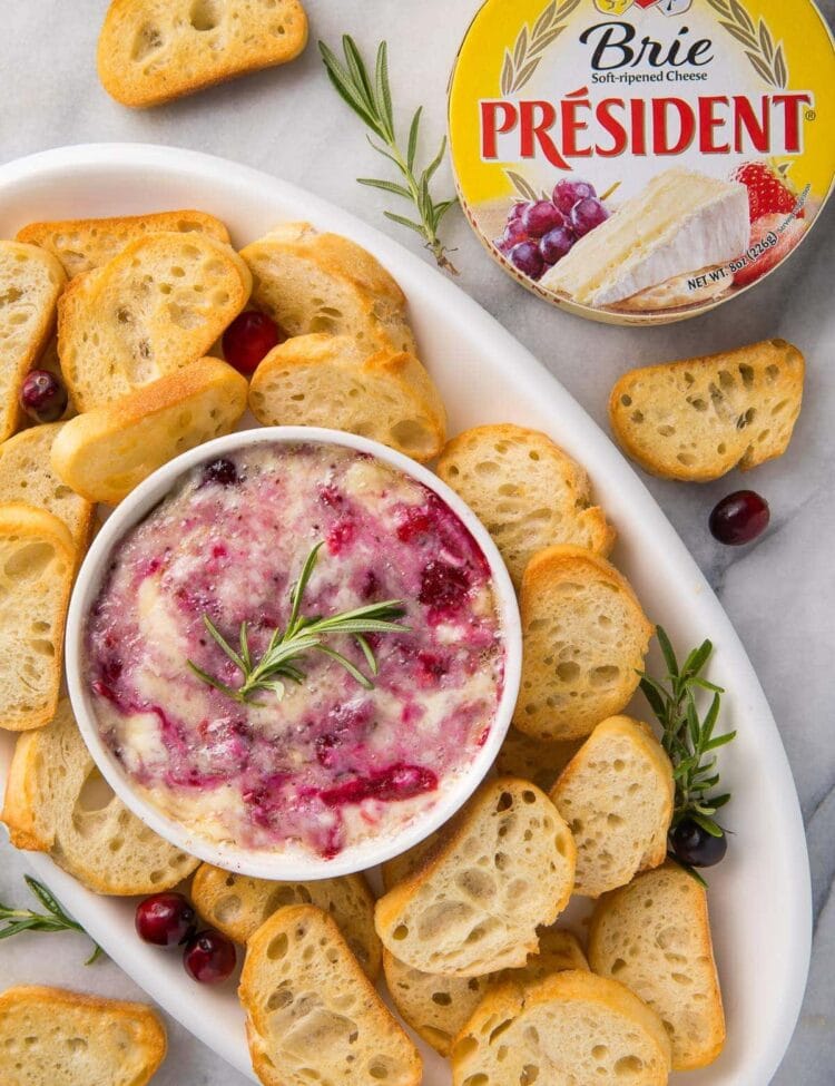 A serving tray with crackers and cranberry brie dip with a package of President Brie
