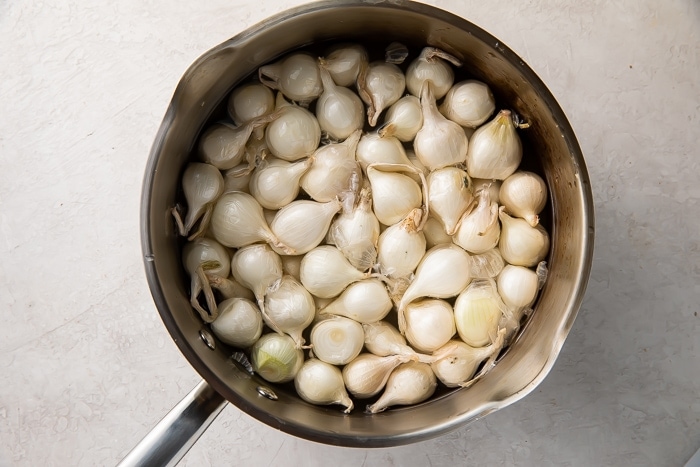 Overhead view of unpeeled pearl onions in a large heavy-bottomed pot.