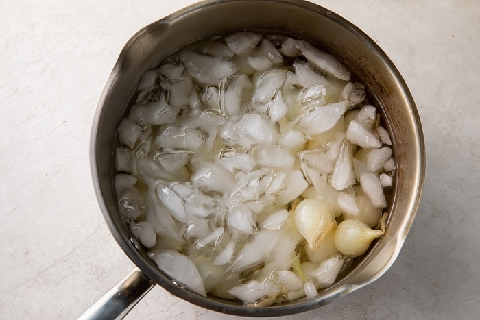 Overhead view of blanched, unpeeled pearl onions in a large heavy-bottomed pot.