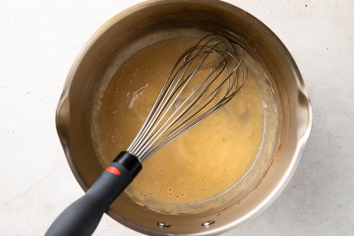 Overhead view of an all-purpose flour and butter roux in a silver saucepan with a silver whisk.