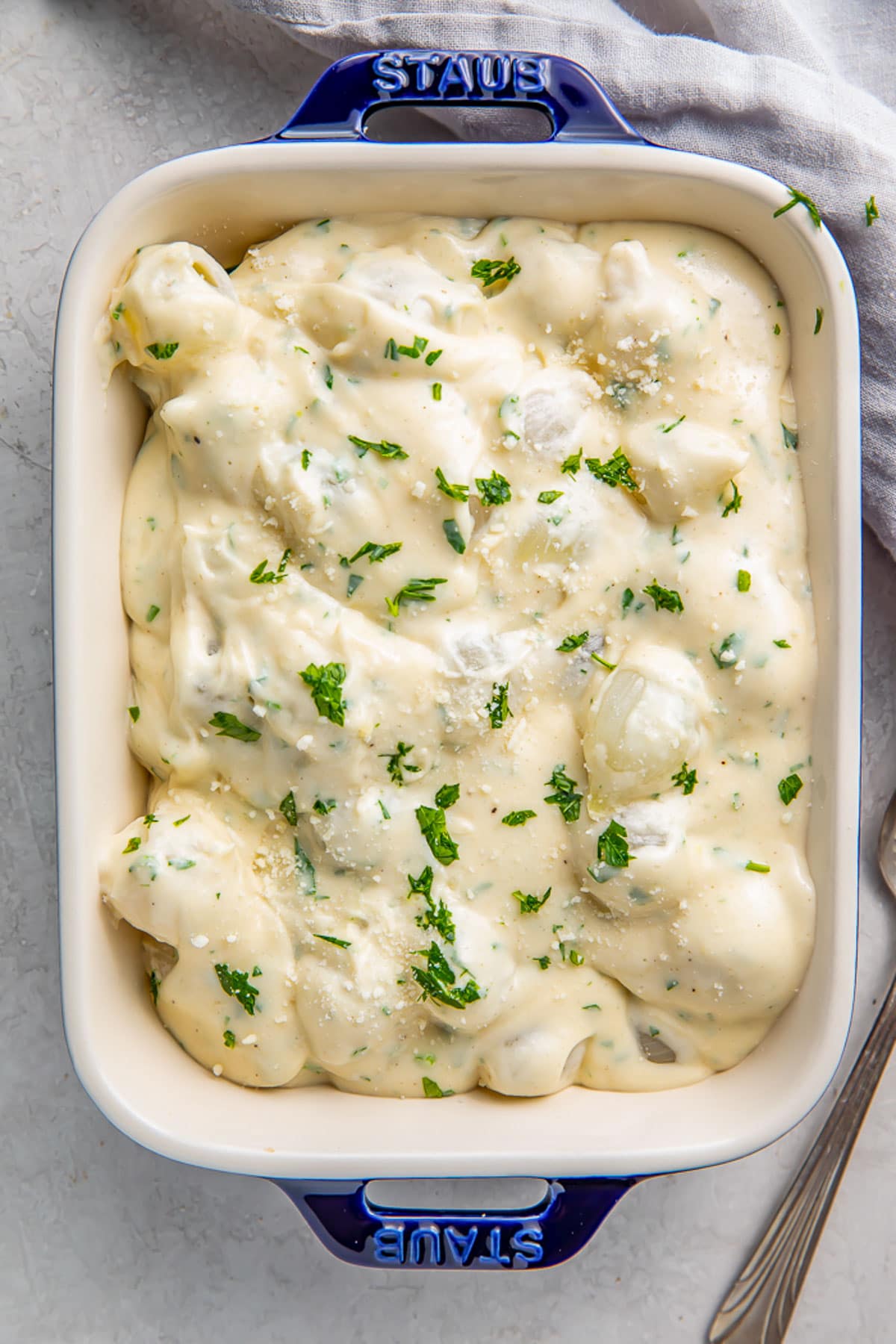 Overhead photo of a casserole dish holding rich creamed onions garnished with fresh herbs.