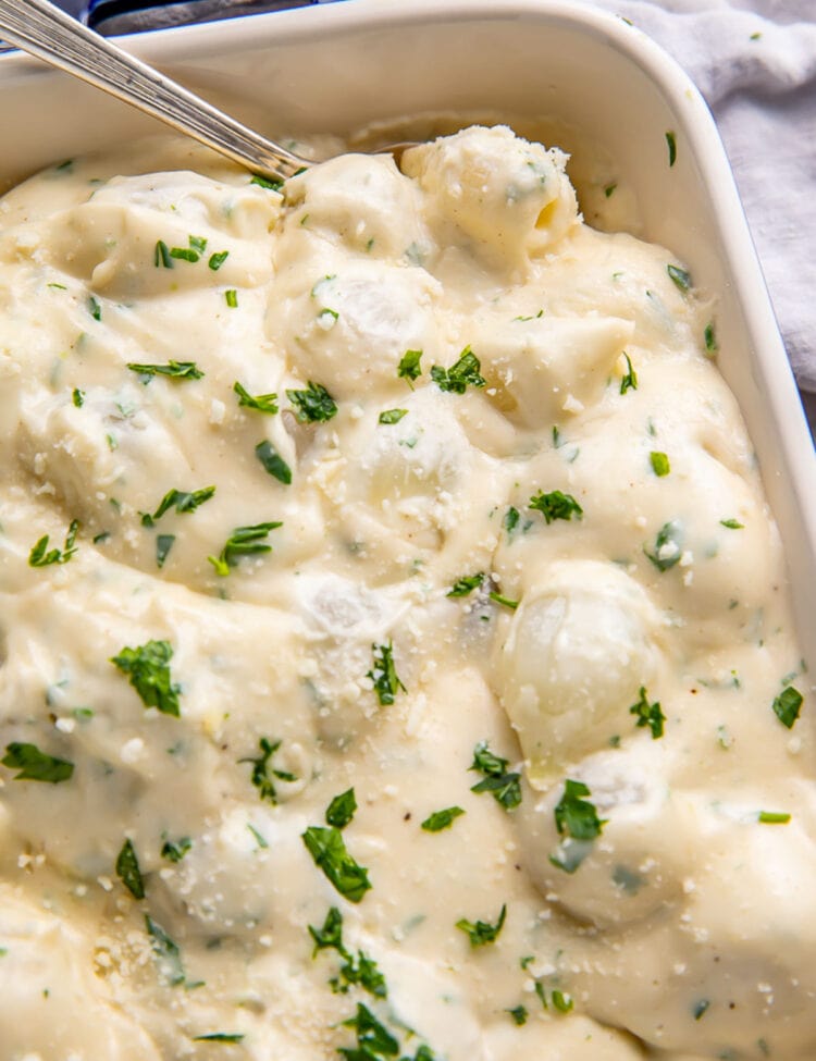 Creamed onions garnished with fresh herbs in a casserole dish.