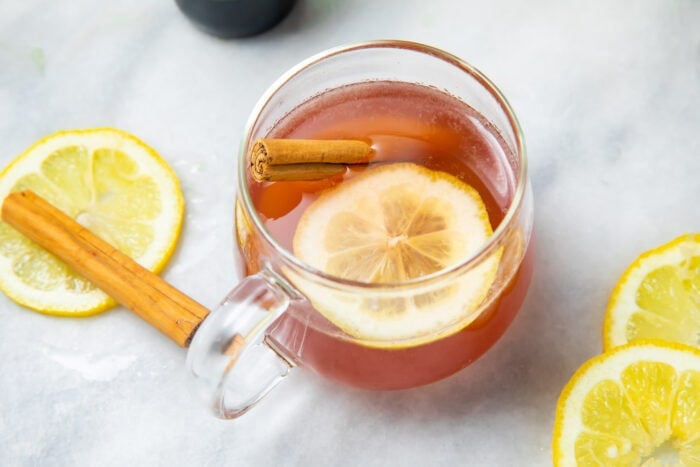 An elderberry hot toddy on a white tablecloth next to a cinnamon stick and lemon slices