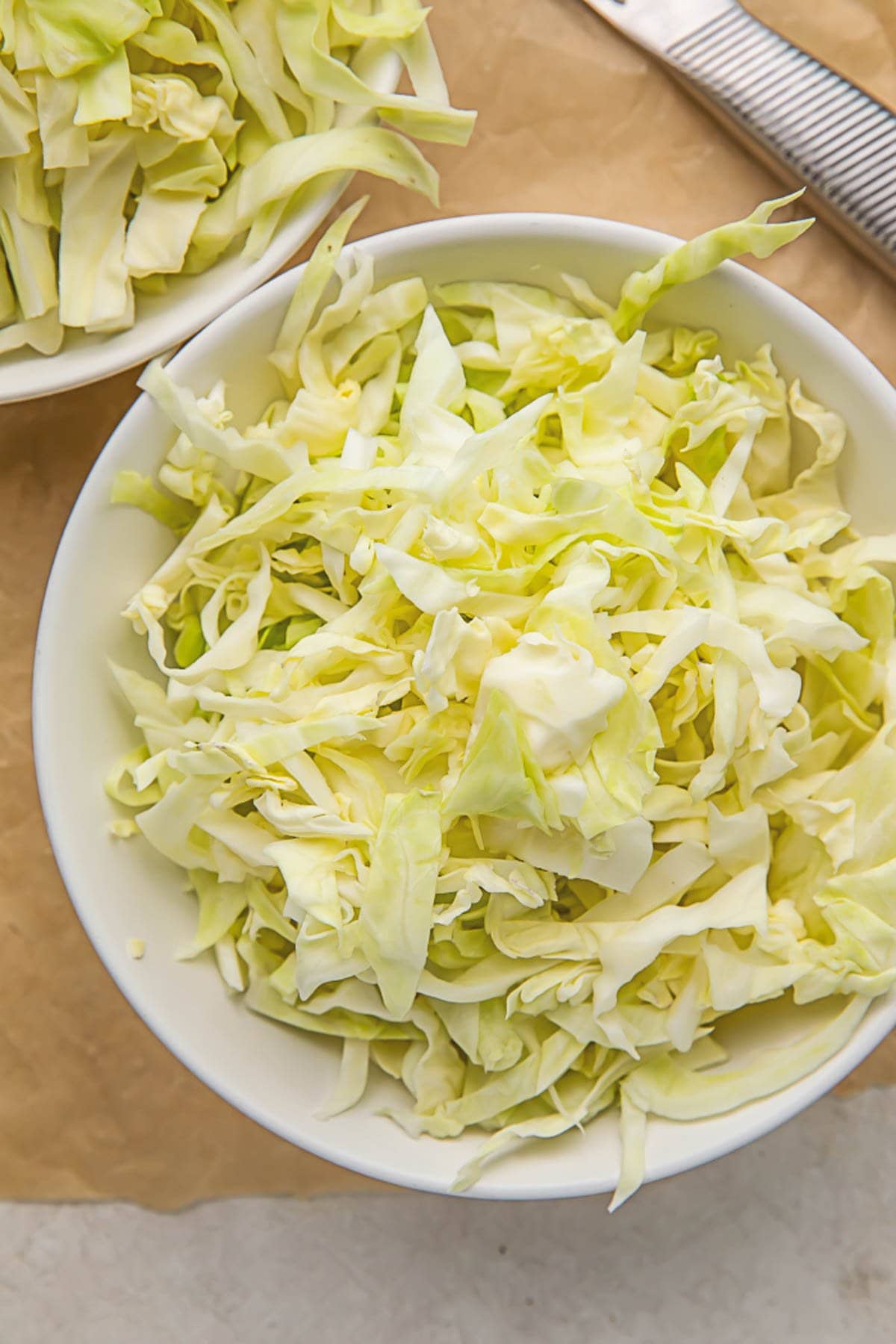 Pieces of shredded cabbage in a white bowl sitting on a wooden cutting board.