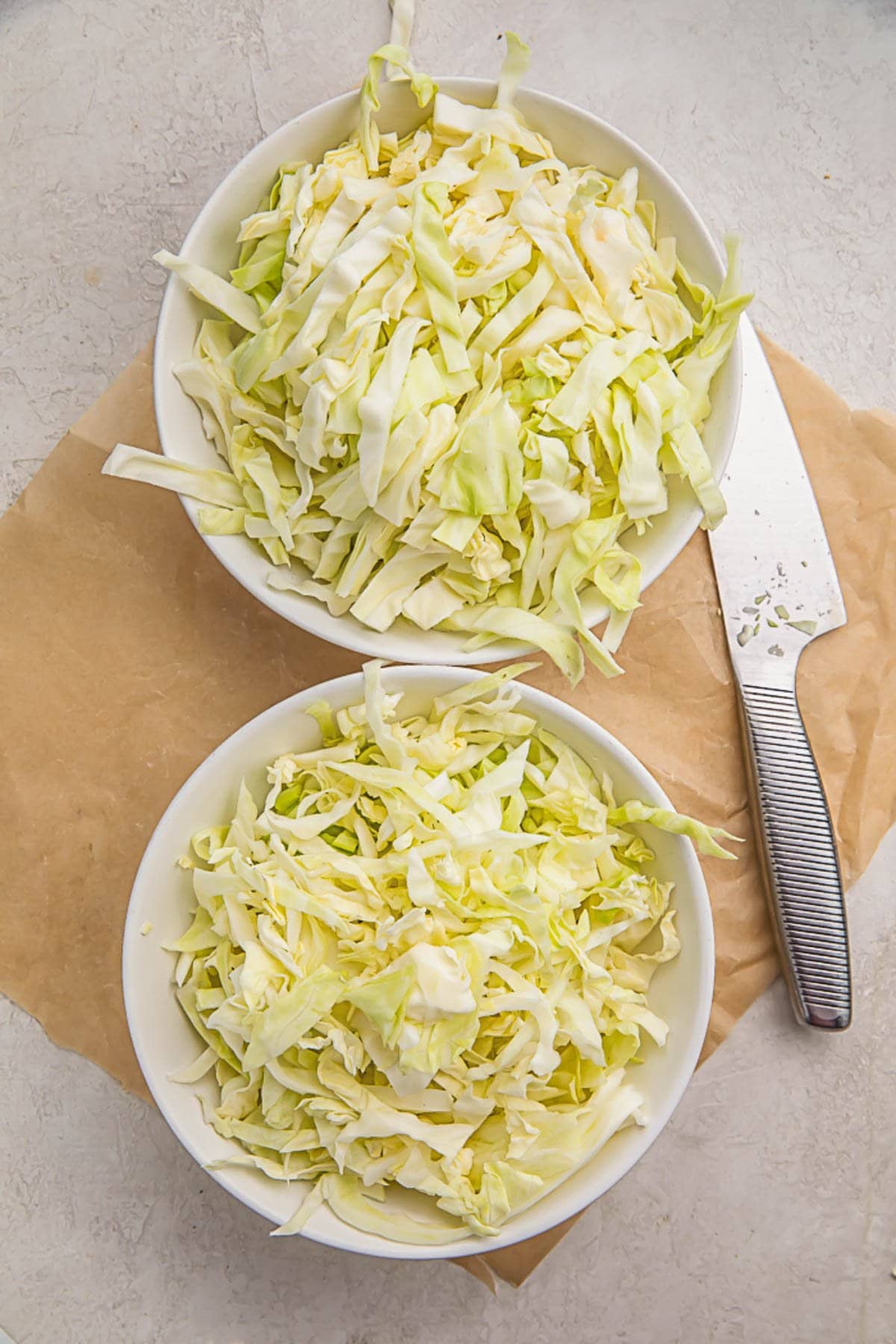Pieces of shredded cabbage in two white bowls sitting on a wooden cutting board.