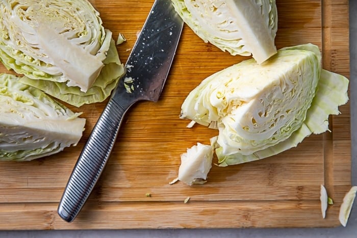 Four wedges of a head of cabbage on a cutting board next to a knife