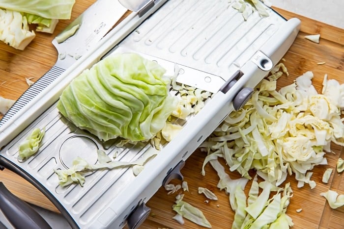 Mandolin with a wedge of cabbage on top and shredded cabbage on a cutting board