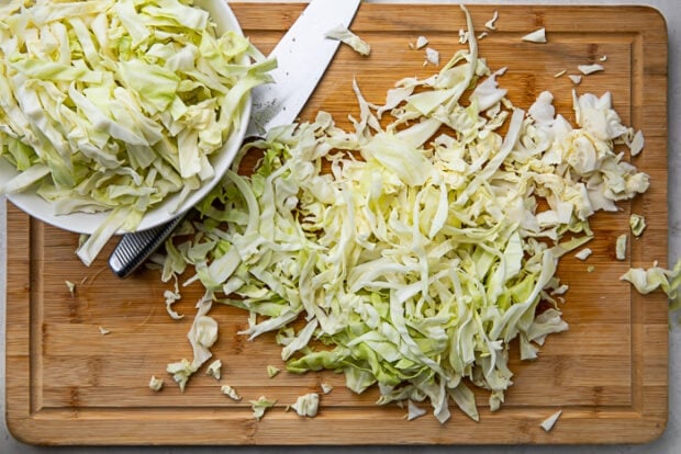 Shredded cabbage on a wooden cutting board next to a knife