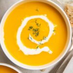 A bowl of butternut squash soup with a drizzle of cream inside a white bowl