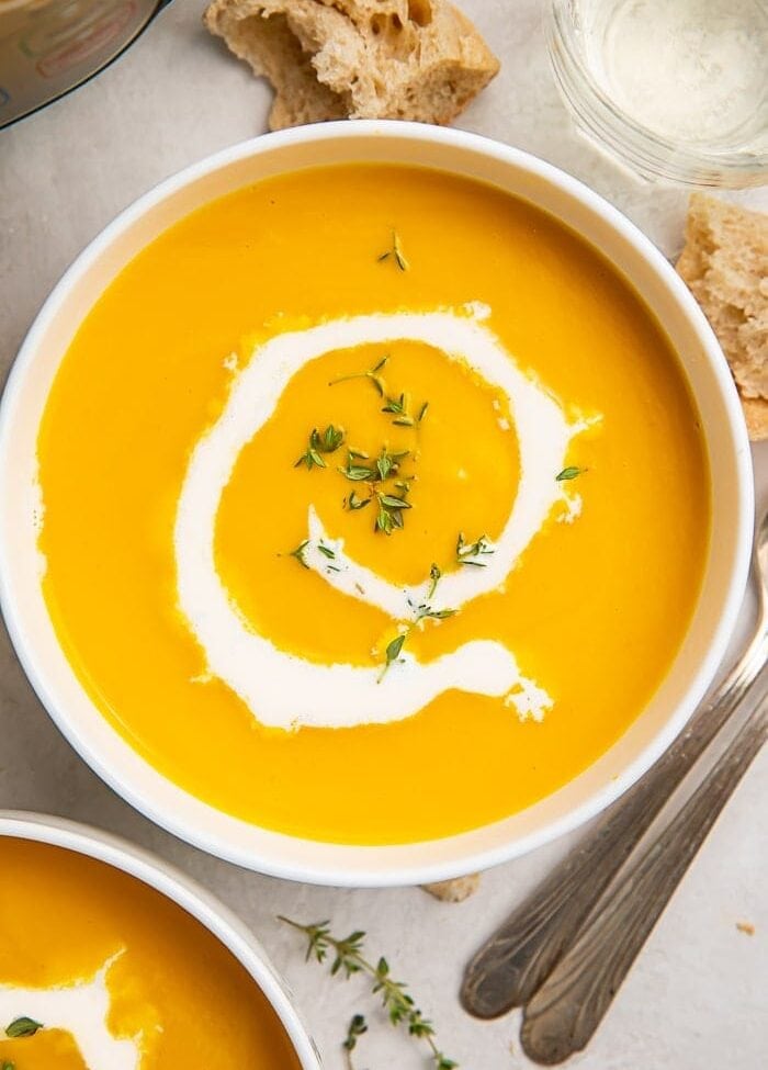 A bowl of butternut squash soup with a drizzle of cream inside a white bowl