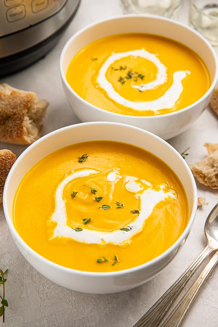Two bowls of butternut squash soup next to spoons and an Instant Pot