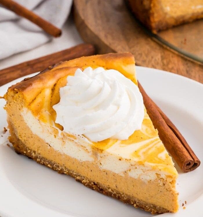 A slice of keto pumpkin cheesecake with a dollop of whipped cream on a white plate with a cinnamon stick