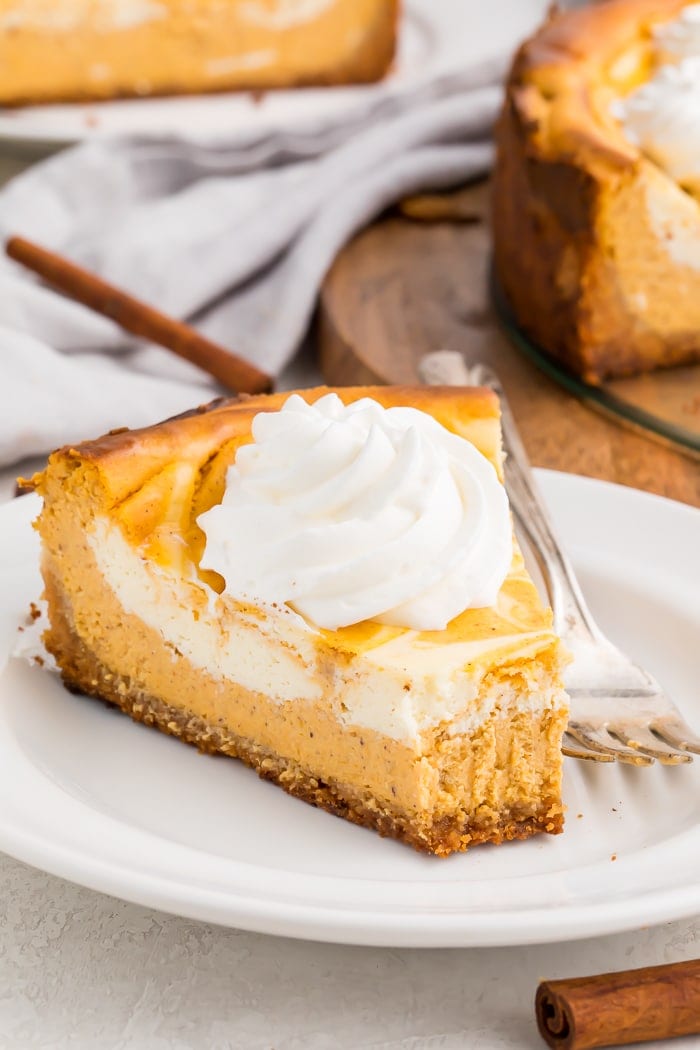 A slice of keto pumpkin cheesecake with a dollop of whipped cream with a bite taken out on a white plate with a fork