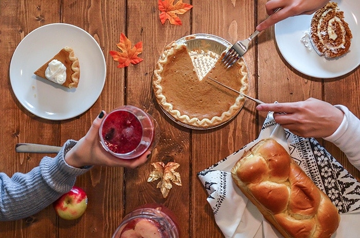 A Thanksgiving table with one hand holding a drink and another cutting a pie