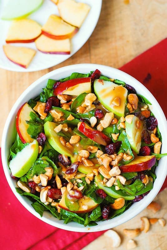 A white bowl full of apple wedges, cranberry, and spinach