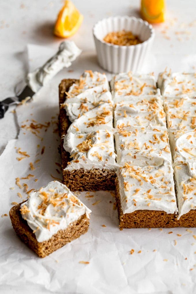 Sheet of spiced chai cake squares with whipped cream frosting and toasted coconut garnish