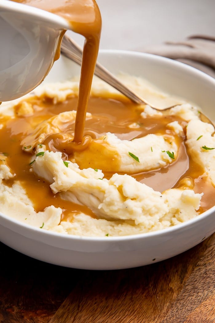 Brown gravy being poured on top of a bowl of mashed potatoes