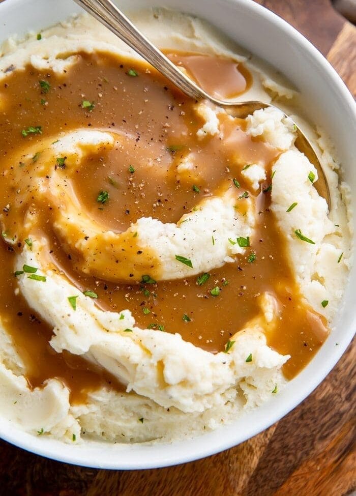 Mashed potatoes in a bowl with a spoon swirled with brown gravy