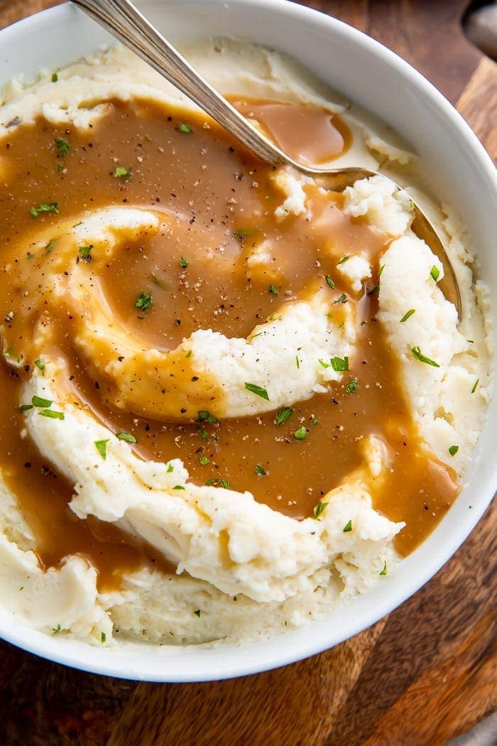 Mashed potatoes in a bowl with a spoon swirled with brown gravy