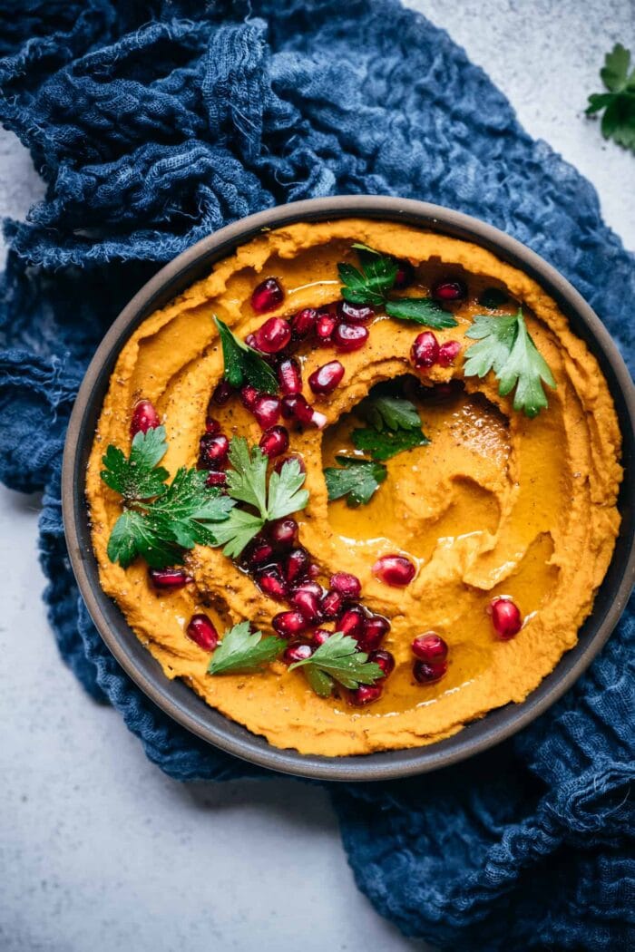 Black cast iron dish with roasted carrot dip, cranberries, and parsley