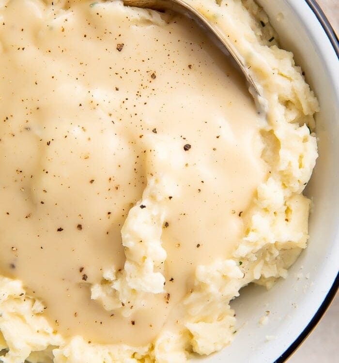 Overhead shot of chicken gravy over mashed potatoes in a white bowl with a spoon