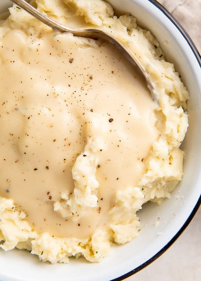 Overhead shot of chicken gravy over mashed potatoes in a white bowl with a spoon