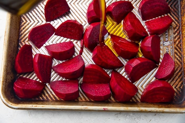 Dark red beet wedges covered with extra virgin olive oil on silver sheet pan