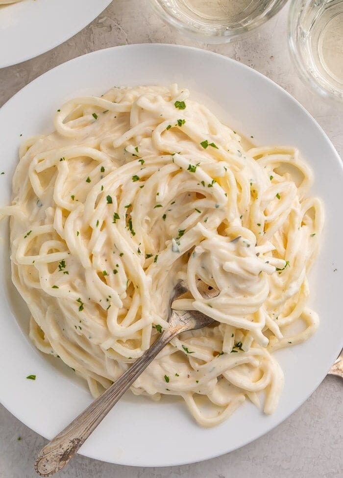 Pasta with keto alfredo sauce on a white plate with a fork